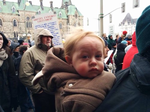 Outside the Canadian Houses of Parliament, a 1-year old, third generation Pagan attends his first protest. [Photo by Marc LeBlanc]