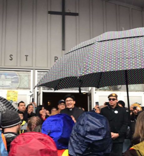 Father Raul, of St Peters Catholic Church, speaks to the crowd and thanks them for coming out in the rain. [Courtesy T.T.Coyle]