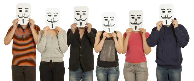 A series of people hold up Guy Fawkes-style masks to obscure their identities.